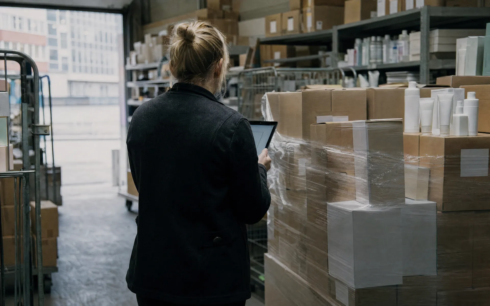 Retail buyer with a tablet checking a delivery of wrapped cartons in a stockroom
