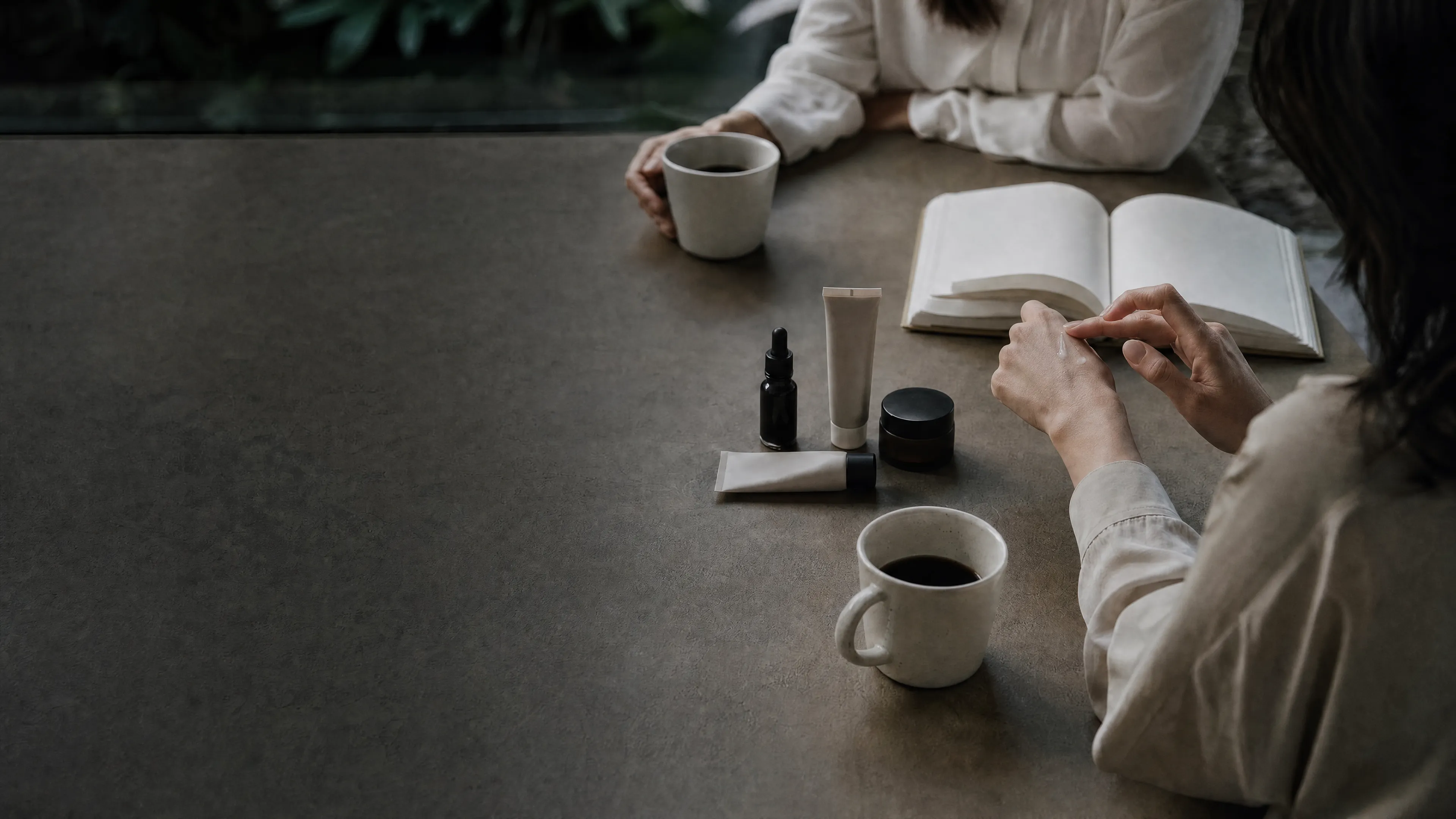 Two people meeting at a stone table with coffee, a notebook and skincare samples