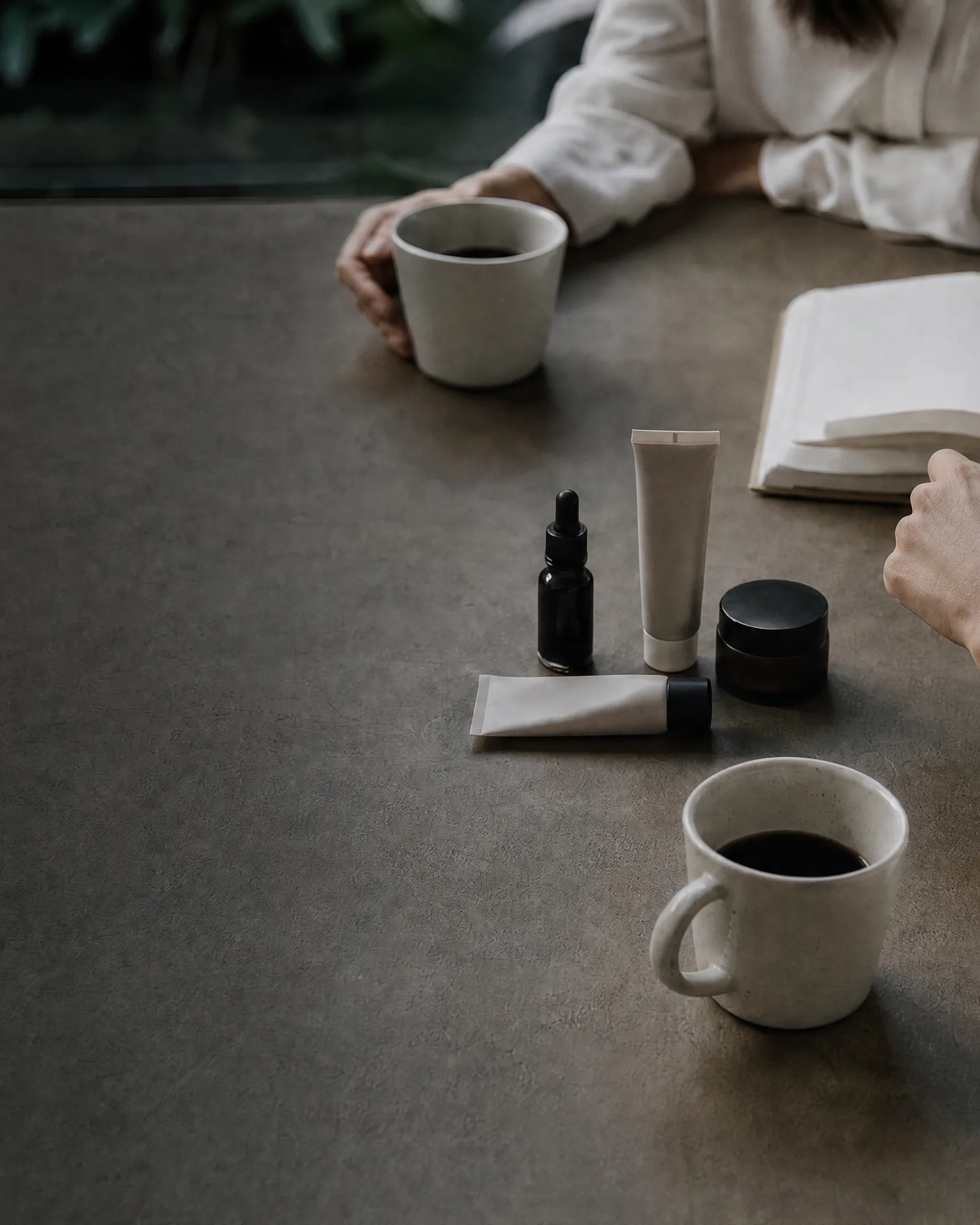 Two people meeting at a stone table with coffee, a notebook and skincare samples